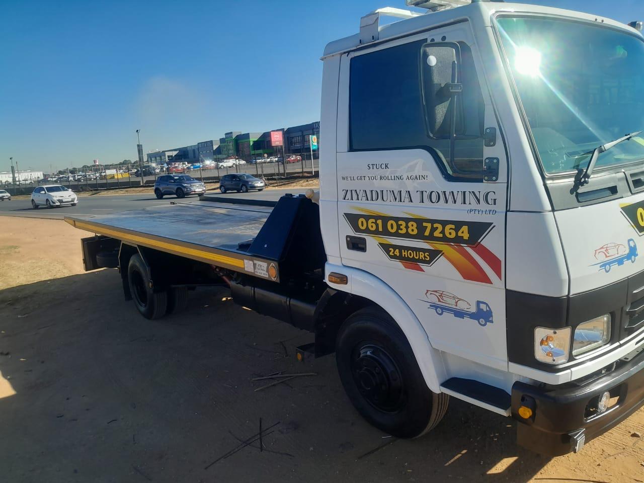 Side view of a Ziyaduma Towing flatbed tow truck with an empty deck